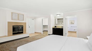 A hotel room with a large bed, a fireplace, a kitchen area, and a bathroom visible through an open door.