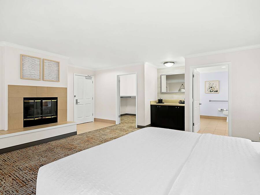 A hotel room with a large bed, a fireplace, a kitchen area, and a bathroom visible through an open door.