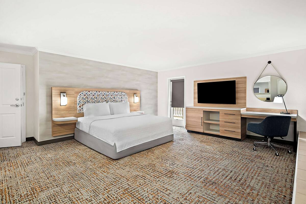 A modern hotel room with a large bed, a desk, a TV, and a mirror.