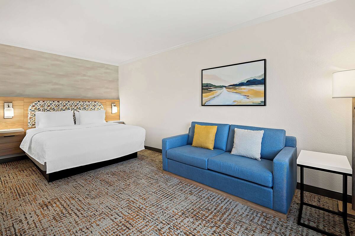 A hotel room with a bed, a blue sofa, a small table, and a painting on the wall.