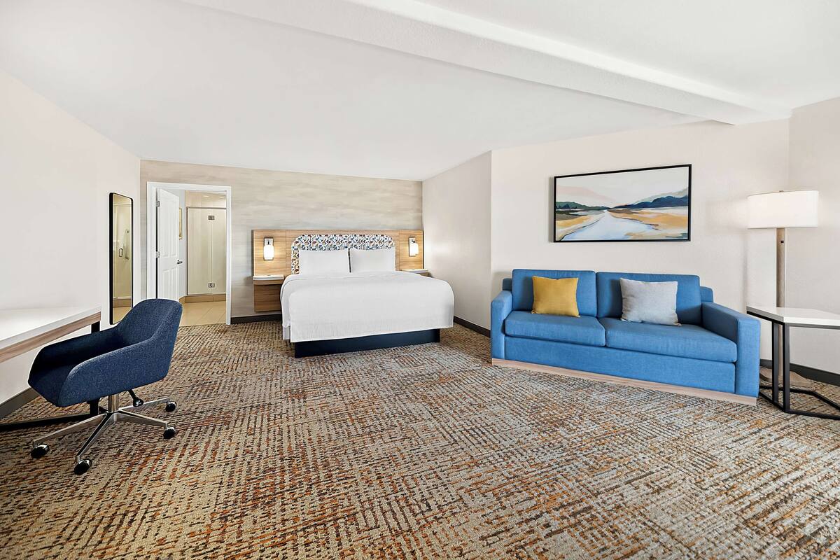 A hotel room with a bed, a blue sofa, a desk, and a chair.