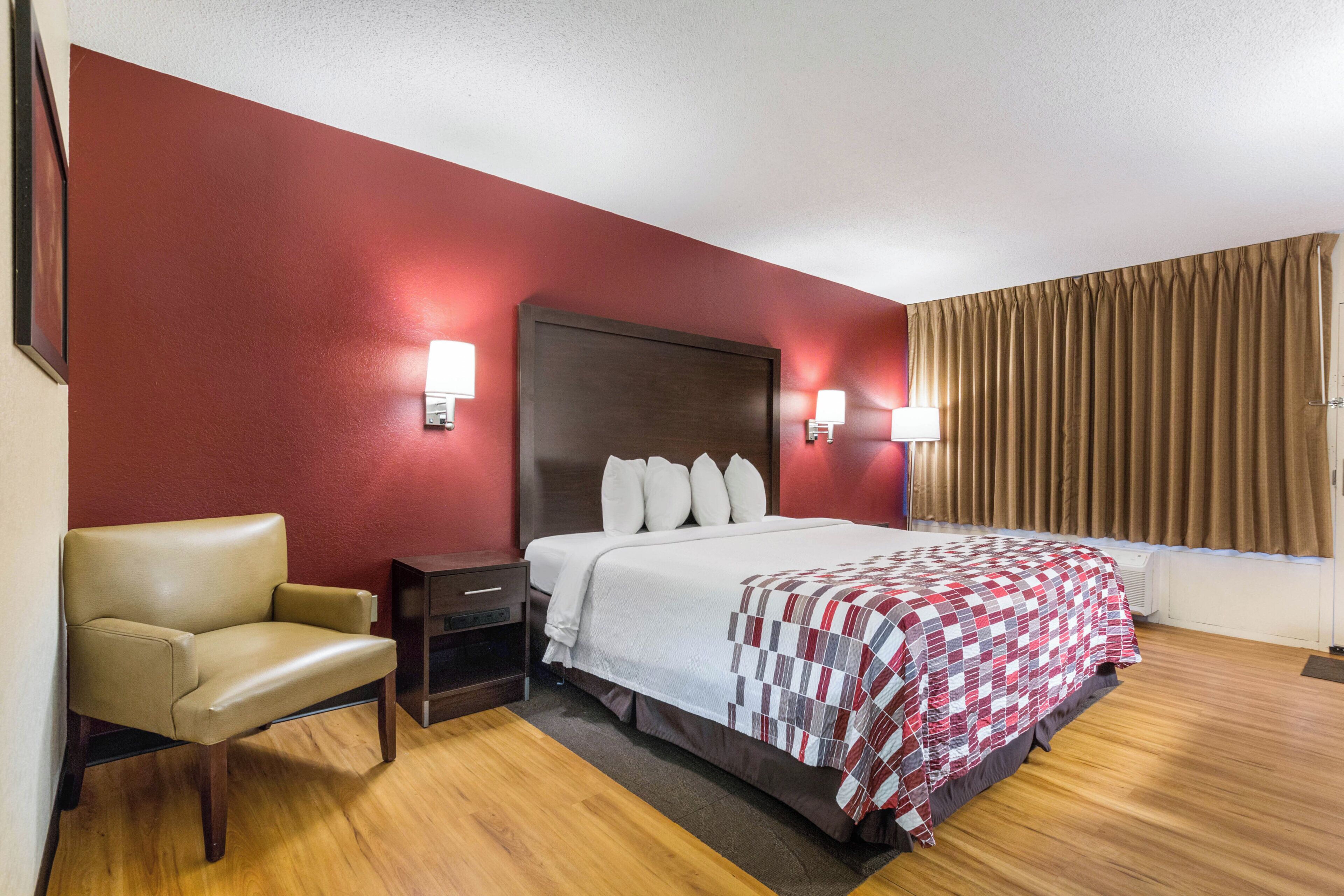 Una habitación de hotel con cama, una silla, una mesita de noche y una ventana con cortinas.
