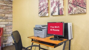 Un escritorio con una impresora Brother, un monitor HP y un letrero que indica Wi-Fi gratuito en todas las habitaciones.