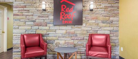 A Red Roof Inn lobby with a stone wall, two red leather chairs, and a small round table.