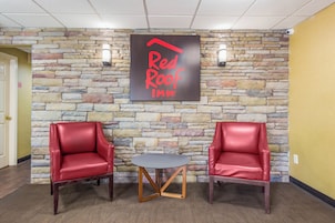 Un vestíbulo de Red Roof Inn con una pared de piedra, dos sillones de cuero rojo y una pequeña mesa redonda.