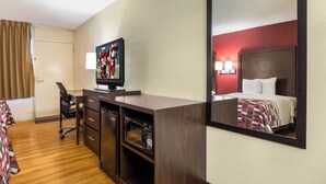 Habitación de hotel con cama, escritorio con computadora, silla, televisor y espejo.