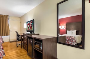 Habitación de hotel con cama, escritorio con computadora, silla, televisor y espejo.