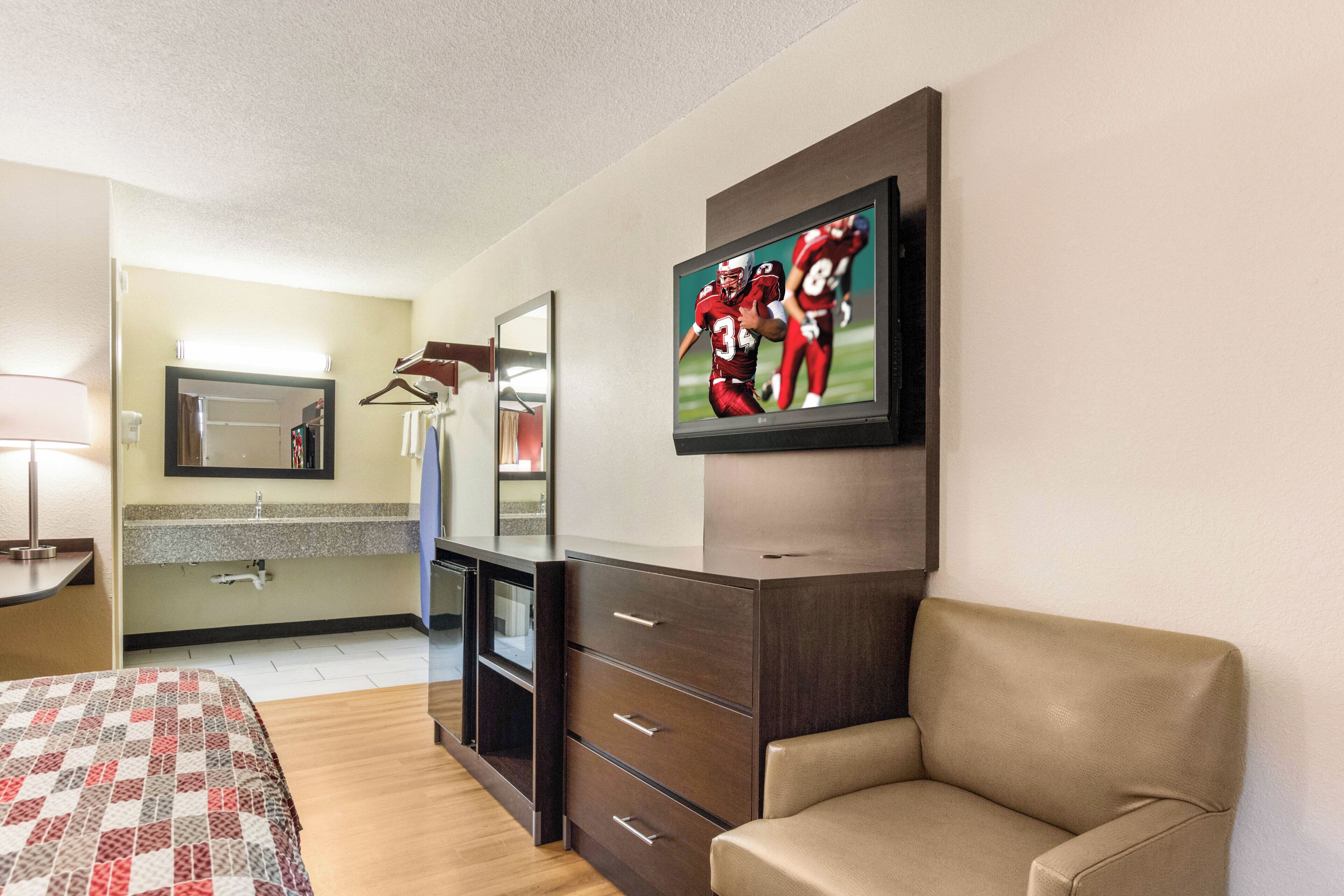A hotel room with a bed, a dresser, a TV, and a mirror.