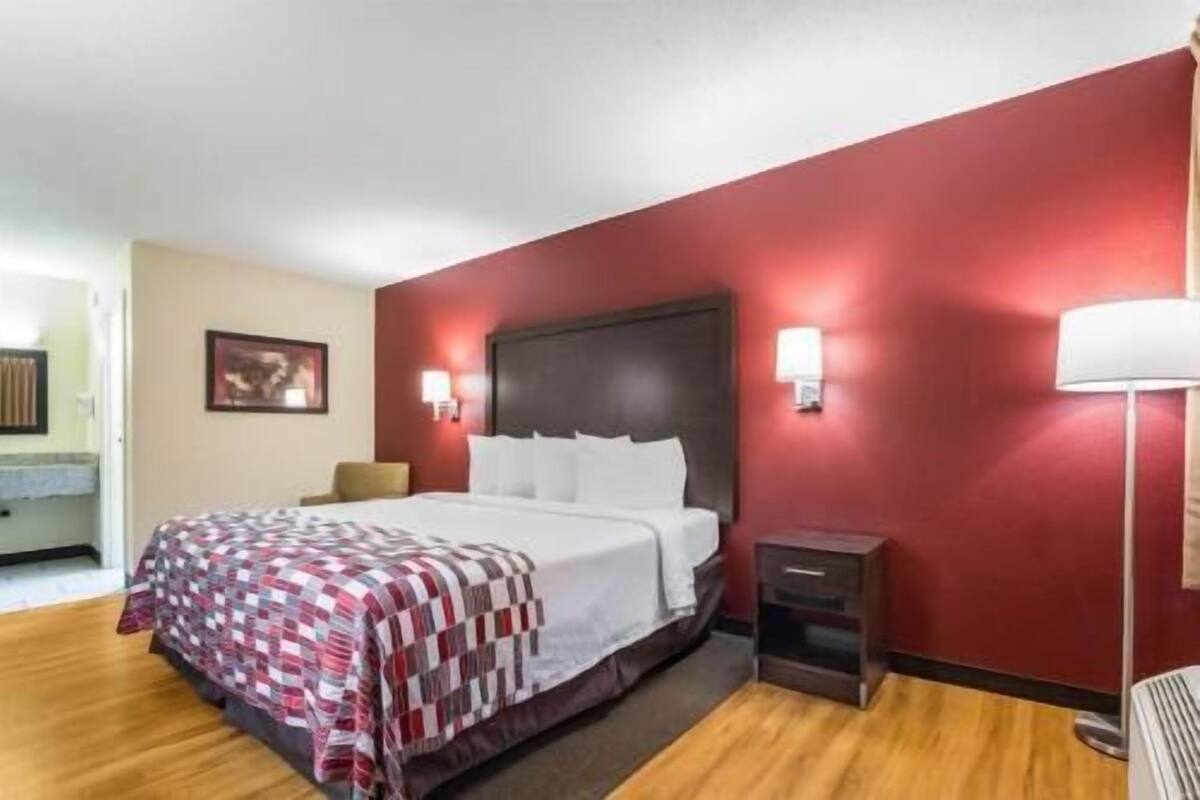 A hotel room with a bed, bedside tables, a red wall, and a framed picture on the wall.