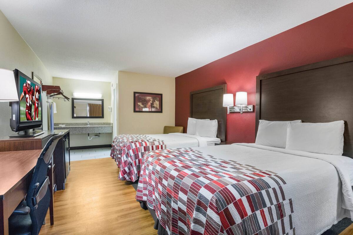 A hotel room with two beds, a desk, a television, and a bathroom.