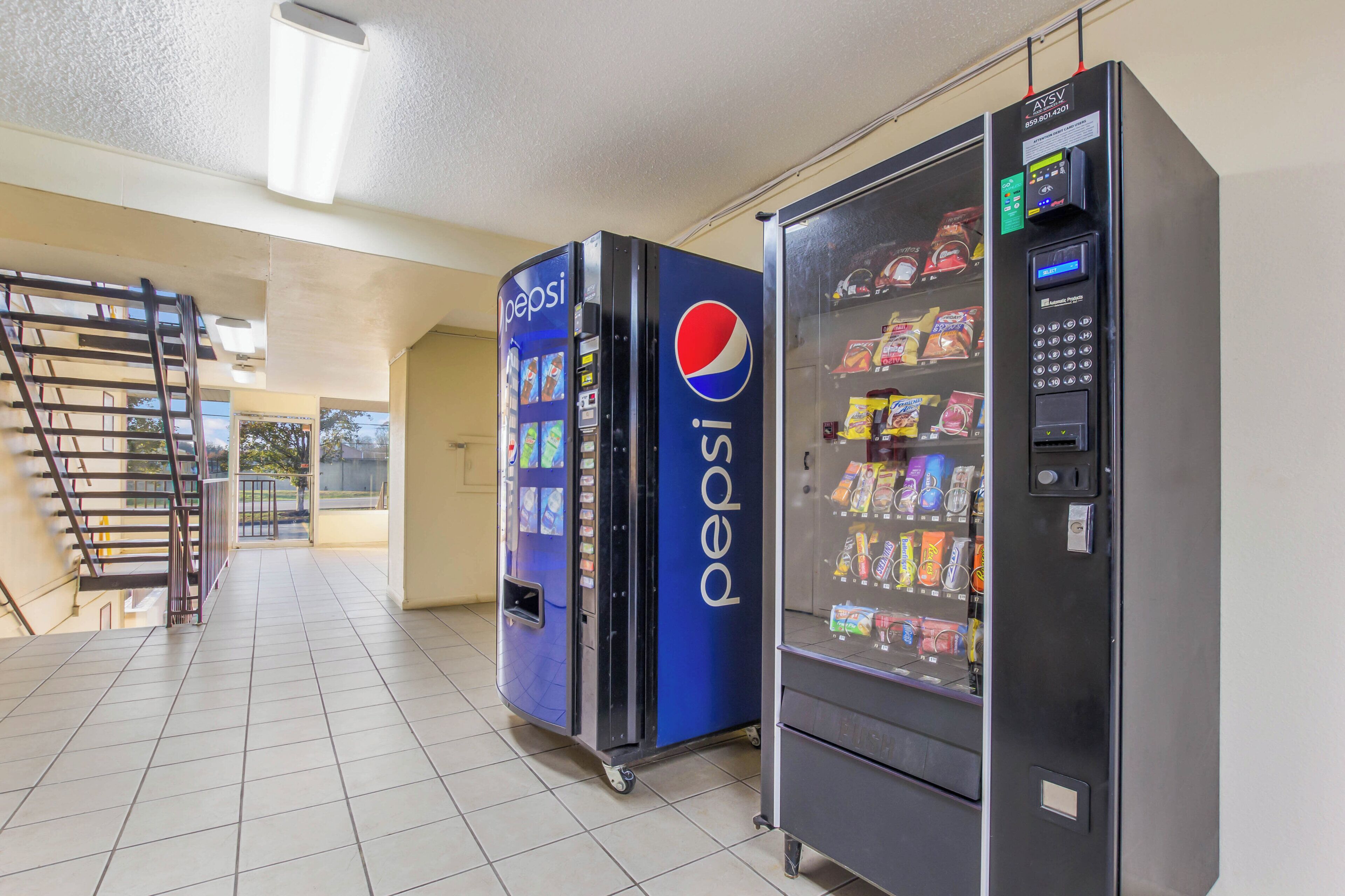 Ein Verkaufsautomatenbereich mit Pepsi- und Fushion-Automaten, eine Metalltreppe und Blick nach draußen.