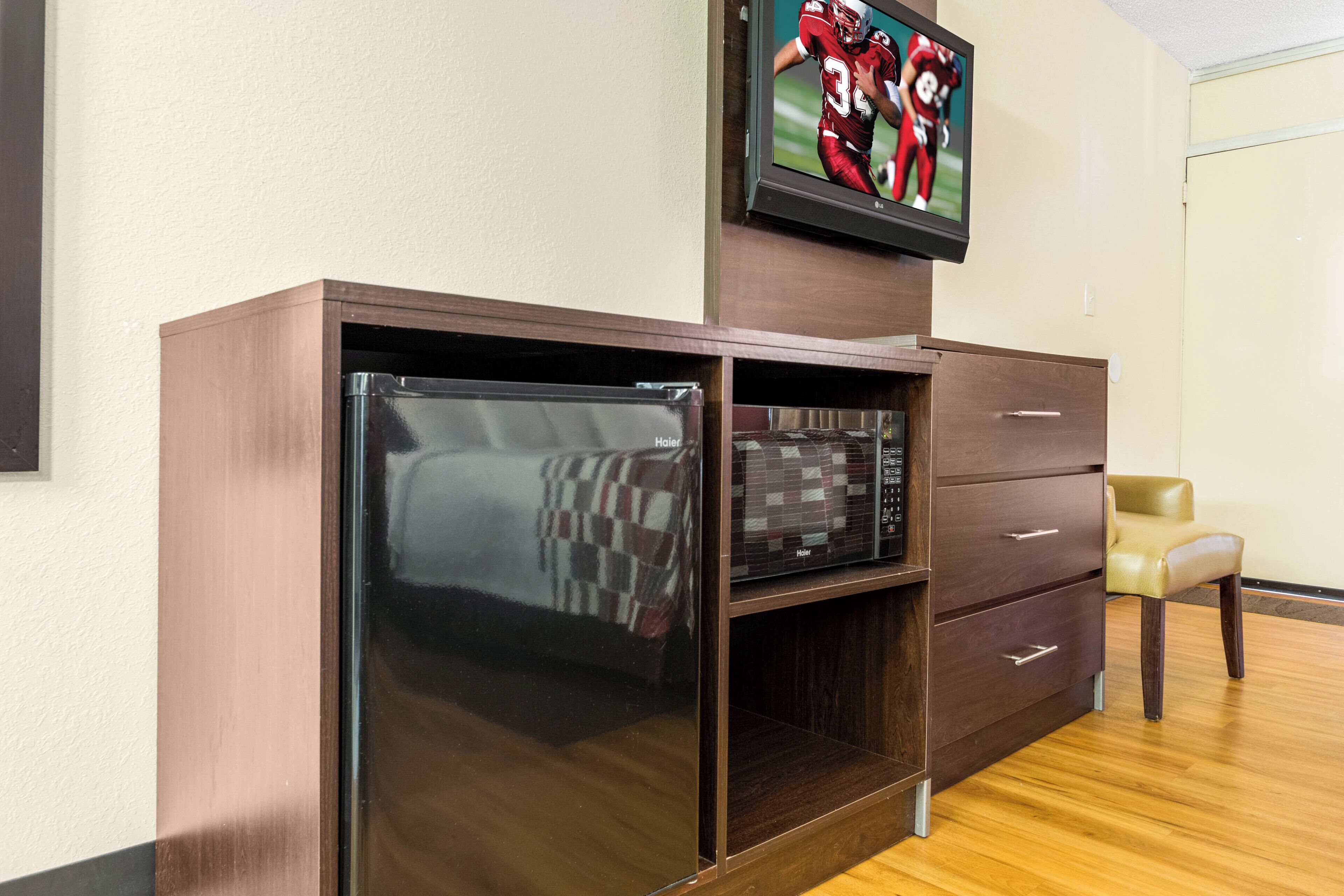 Una habitación con un armario de madera, un televisor montado encima y una silla.
