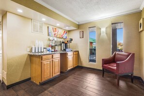 A hotel room with a kitchenette, a red leather chair, and a window with a view of the outside.