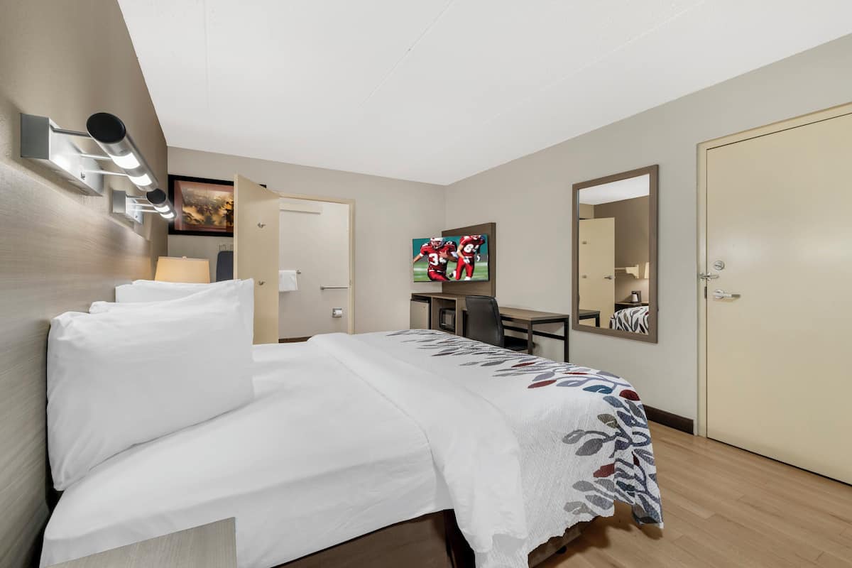 Ein Hotelzimmer mit Bett, Schreibtisch, Stuhl, Spiegel und Tür.