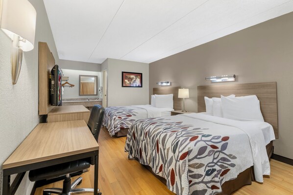 A hotel room with two beds, a desk, a chair, a mirror, and a wall-mounted lamp. - Red Roof Inn Buffalo - Niagara Airport (Bowmansville)