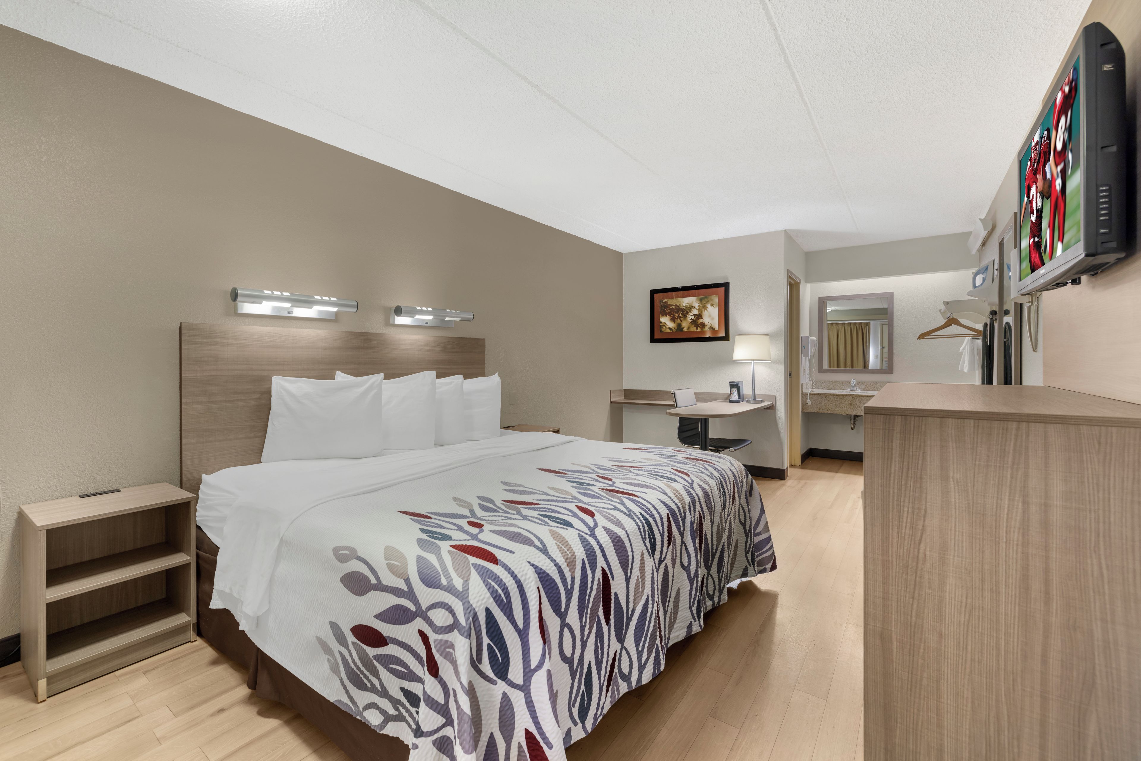 A hotel room with a bed, bedside tables, a desk, a mirror, and a television.