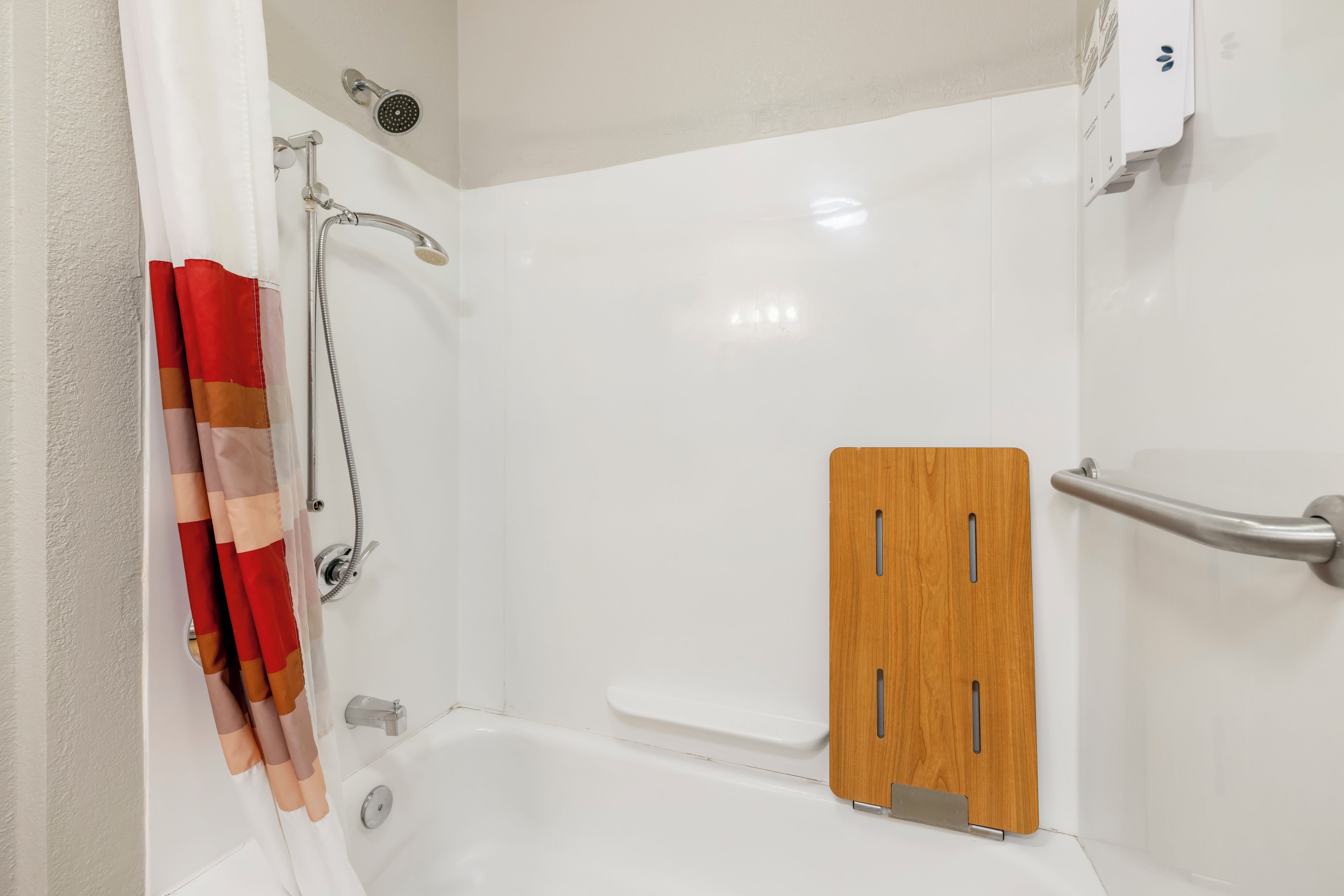 A shower area with a white bathtub, a wooden panel, and a metal grab bar.