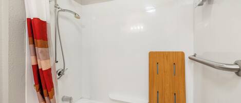 A shower area with a white bathtub, a wooden panel, and a metal grab bar.