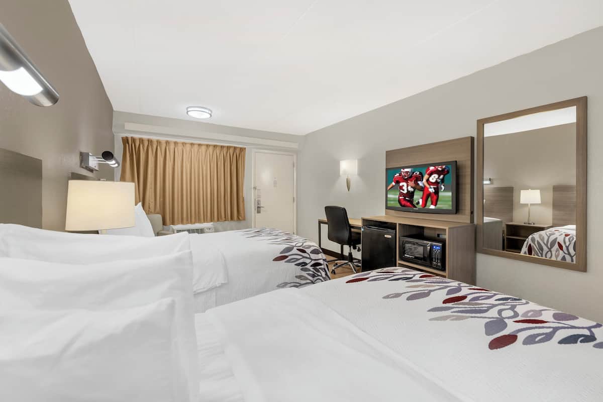 Ein Hotelzimmer mit zwei Betten, einem Schreibtisch, einem Fernseher und einem Spiegel.