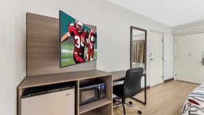 Une chambre d’hôtel équipée d’un téléviseur à écran plat fixé au mur, d’un bureau avec une chaise, d’un four à micro-ondes et d’une armoire.