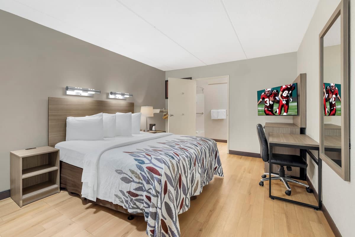 Ein modernes Hotelzimmer mit Bett, Nachttisch, Schreibtisch, Stuhl und einem großen Spiegel.
