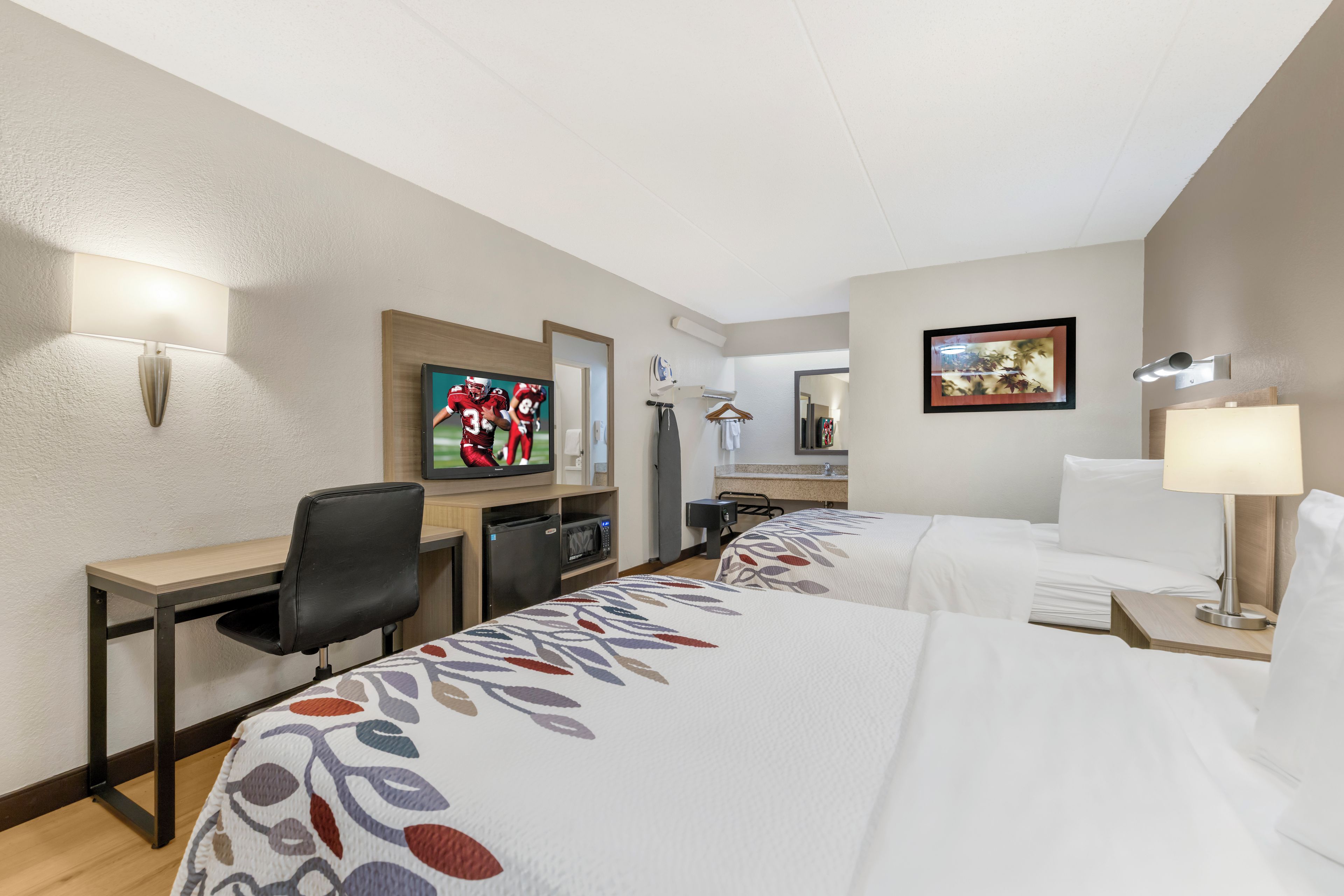 A hotel room with a bed, a desk, a chair, a television, a mirror, a lamp, and a picture on the wall.