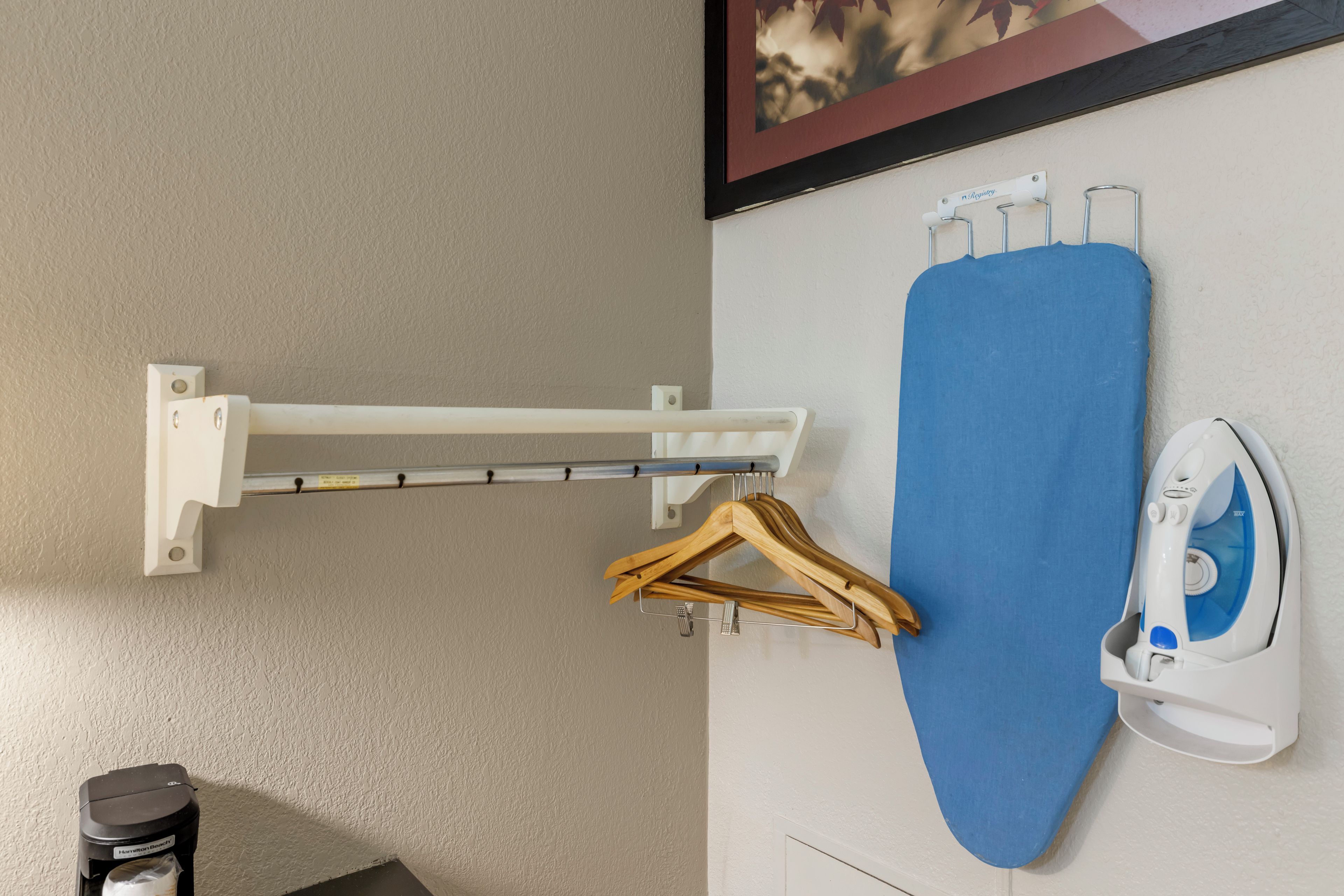 A wall-mounted ironing board with an iron and a wooden hanger.