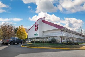 Ett Red Roof Inn-hotell med vit fasad och rött tak, beläget intill en väg där en lastbil står parkerad.
