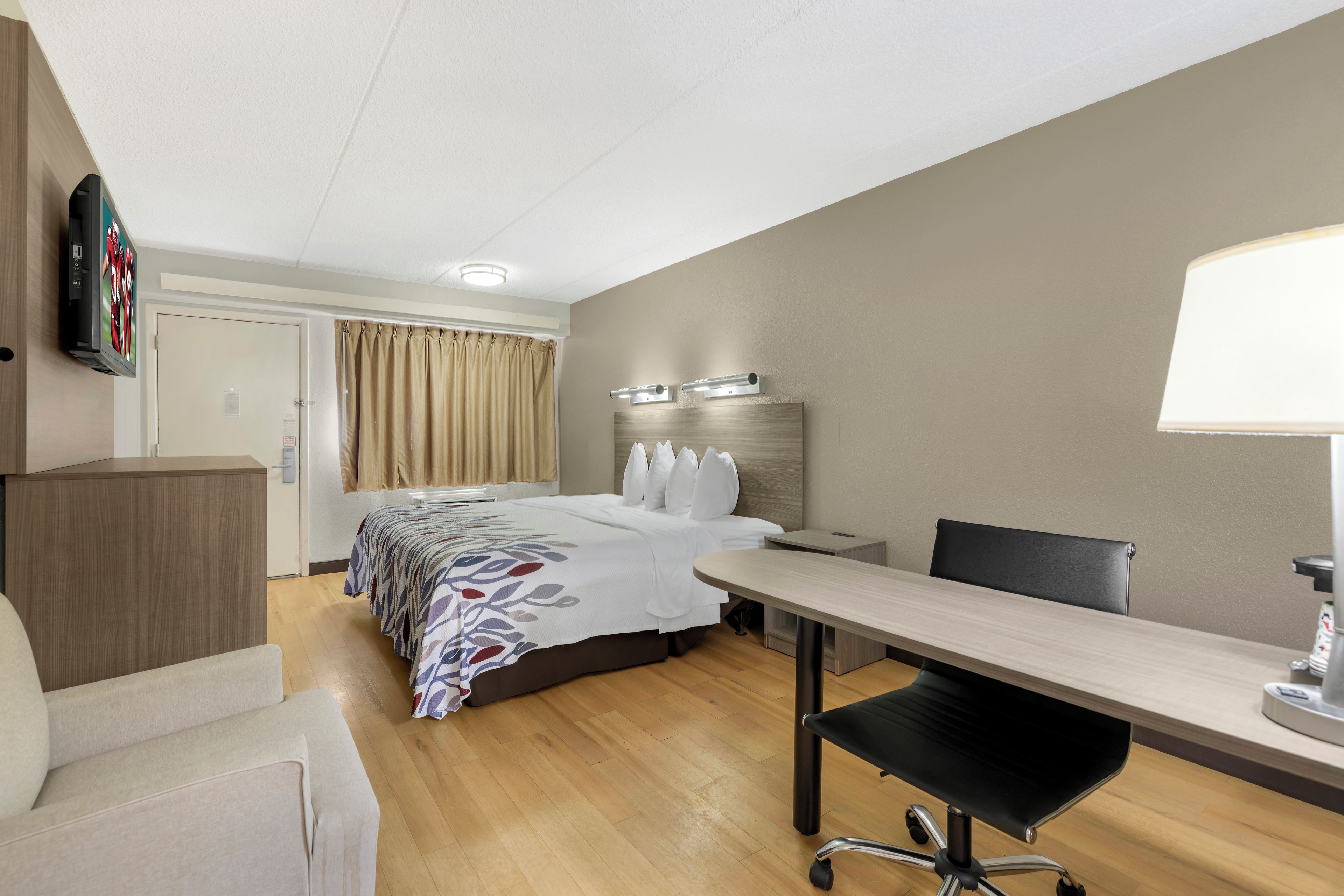 A hotel room with a bed, bedside table, desk, chair, and a television mounted on the wall.