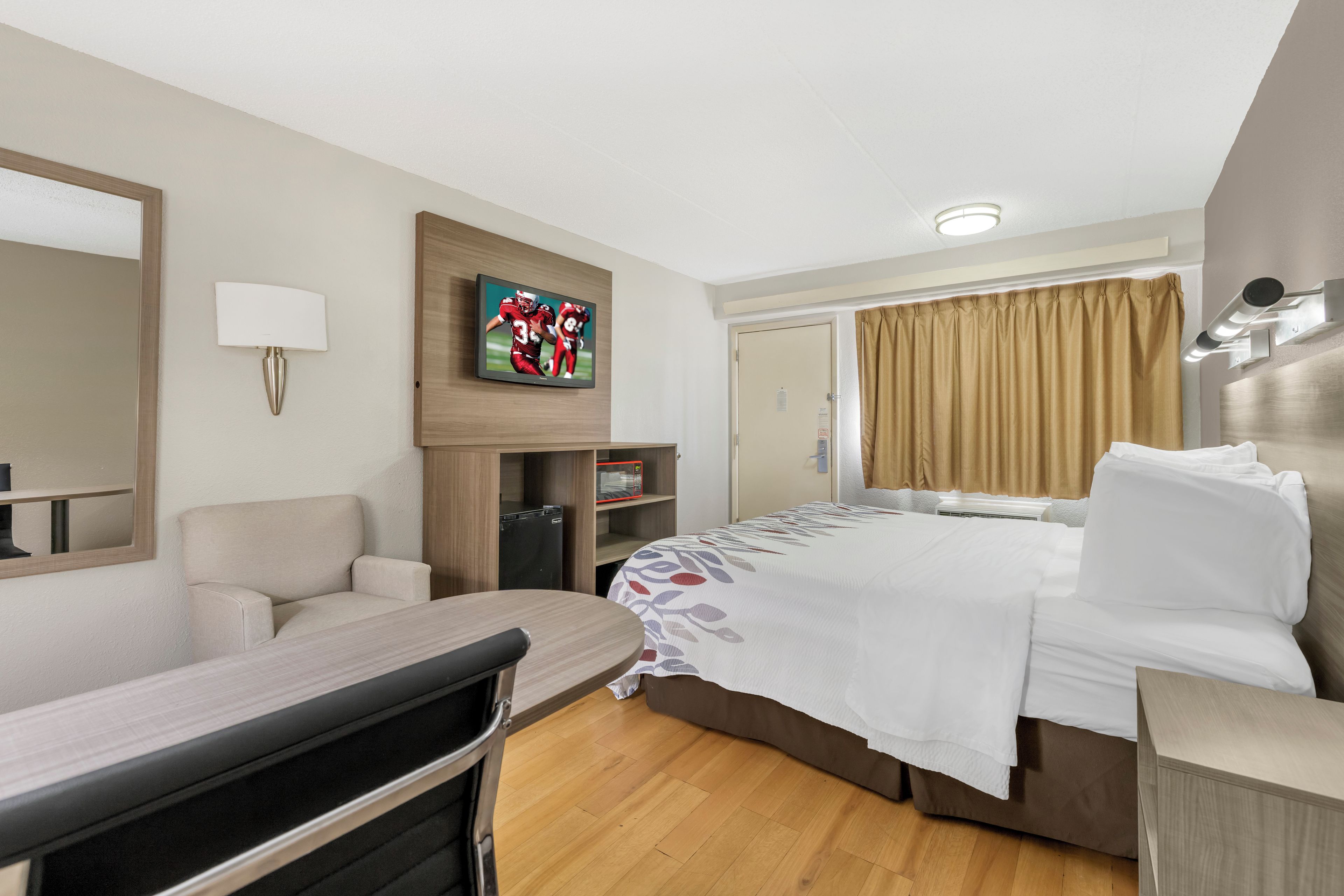Ein Hotelzimmer mit einem Bett, einem Schreibtisch, einem Sessel, einem Fernseher, einer Mikrowelle und einem Kleiderschrank.