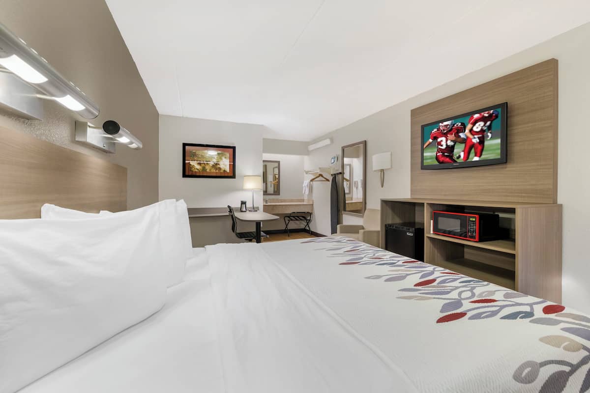 Ein Hotelzimmer mit Bett, Schreibtisch, Stuhl, Fernseher und Mikrowelle.