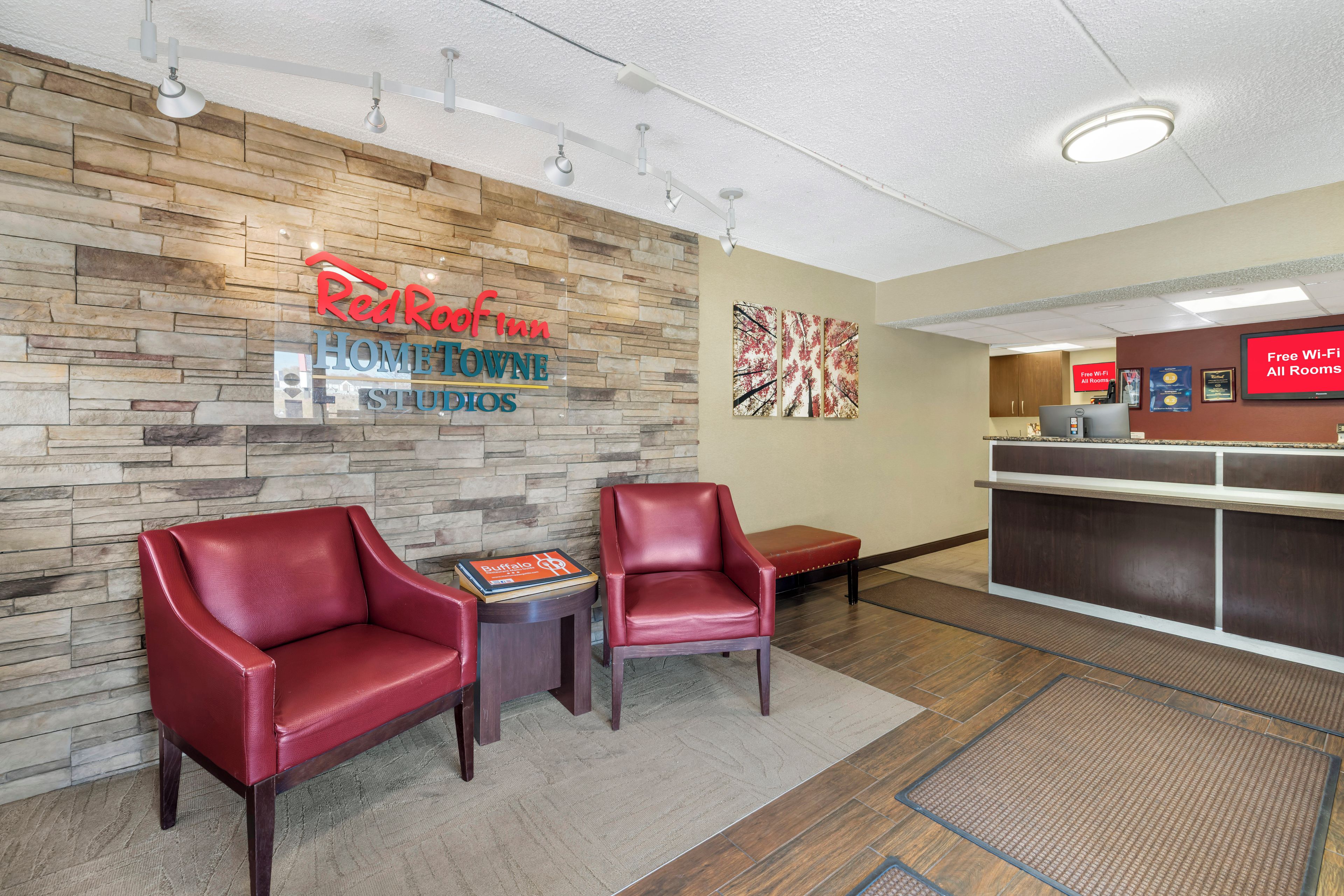 A Red Roof Inn reception area with stone wall decor, two leather chairs, a small table with a brochure, and a digital screen advertising free Wi-Fi.