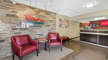 A Red Roof Inn reception area with stone wall decor, two leather chairs, a small table with a brochure, and a digital screen advertising free Wi-Fi.