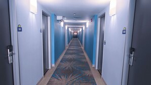 Ein Hotelgang mit blauen Wänden, nummerierten Türen und einem gemusterten Teppich.