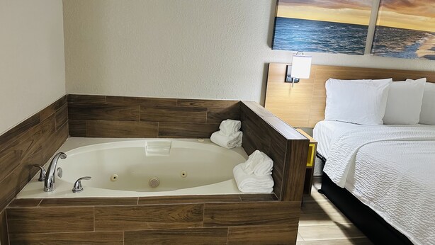 Ein Hotelzimmer mit einer Holzwanne, einem Bett mit weißer Bettwäsche und einem Gemälde, das einen Sonnenuntergang über dem Meer zeigt.