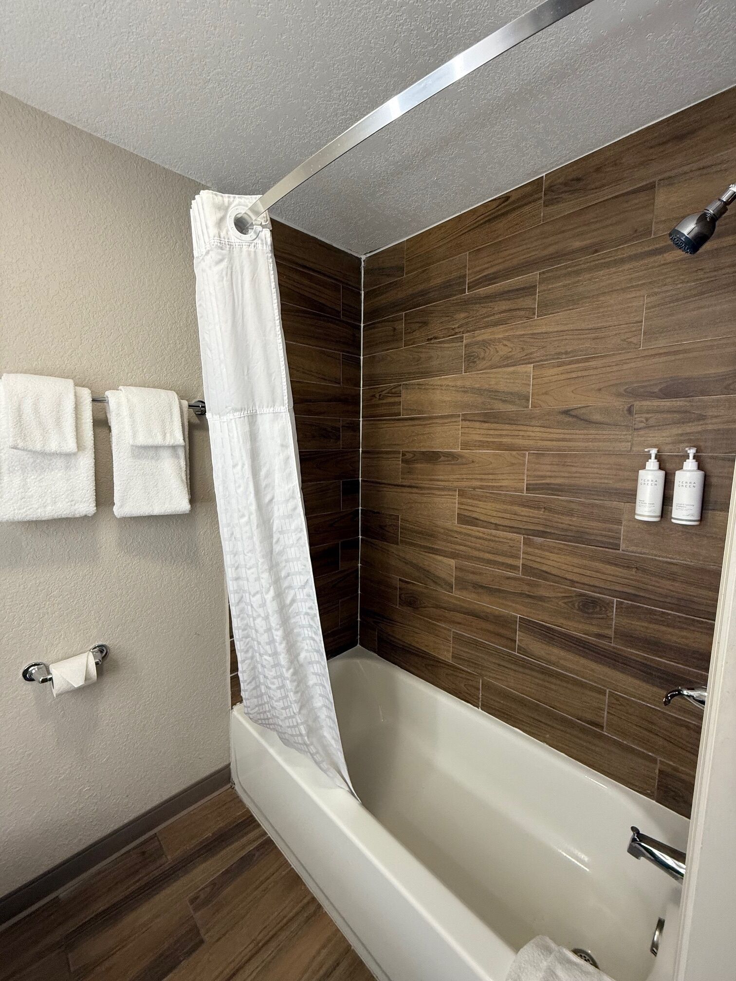 A modern bathroom with a wooden wall, a white bathtub, and two bottles of shampoo on the wall.