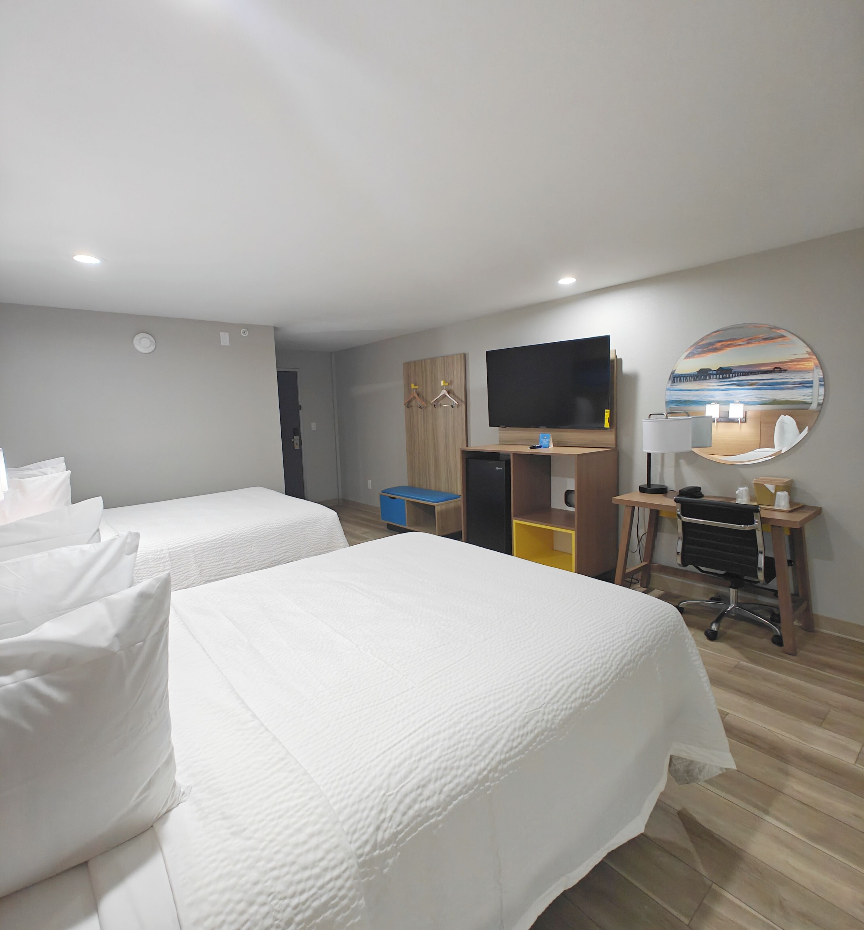A hotel room with two beds, a desk, a chair, a TV, and a large window with a view.