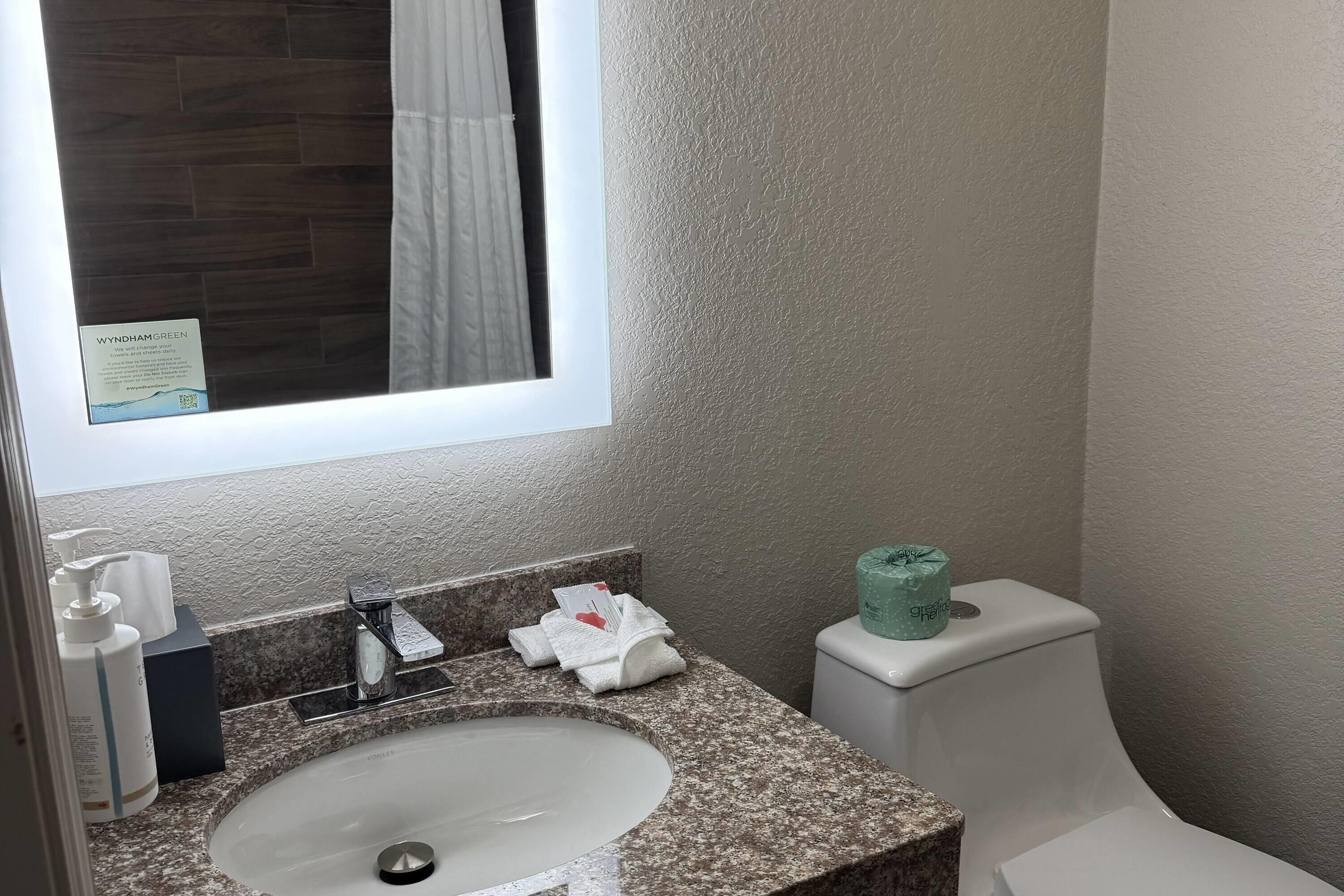Een badkamer met een granieten aanrecht, een wastafel, een toilet en een raam met gordijn.