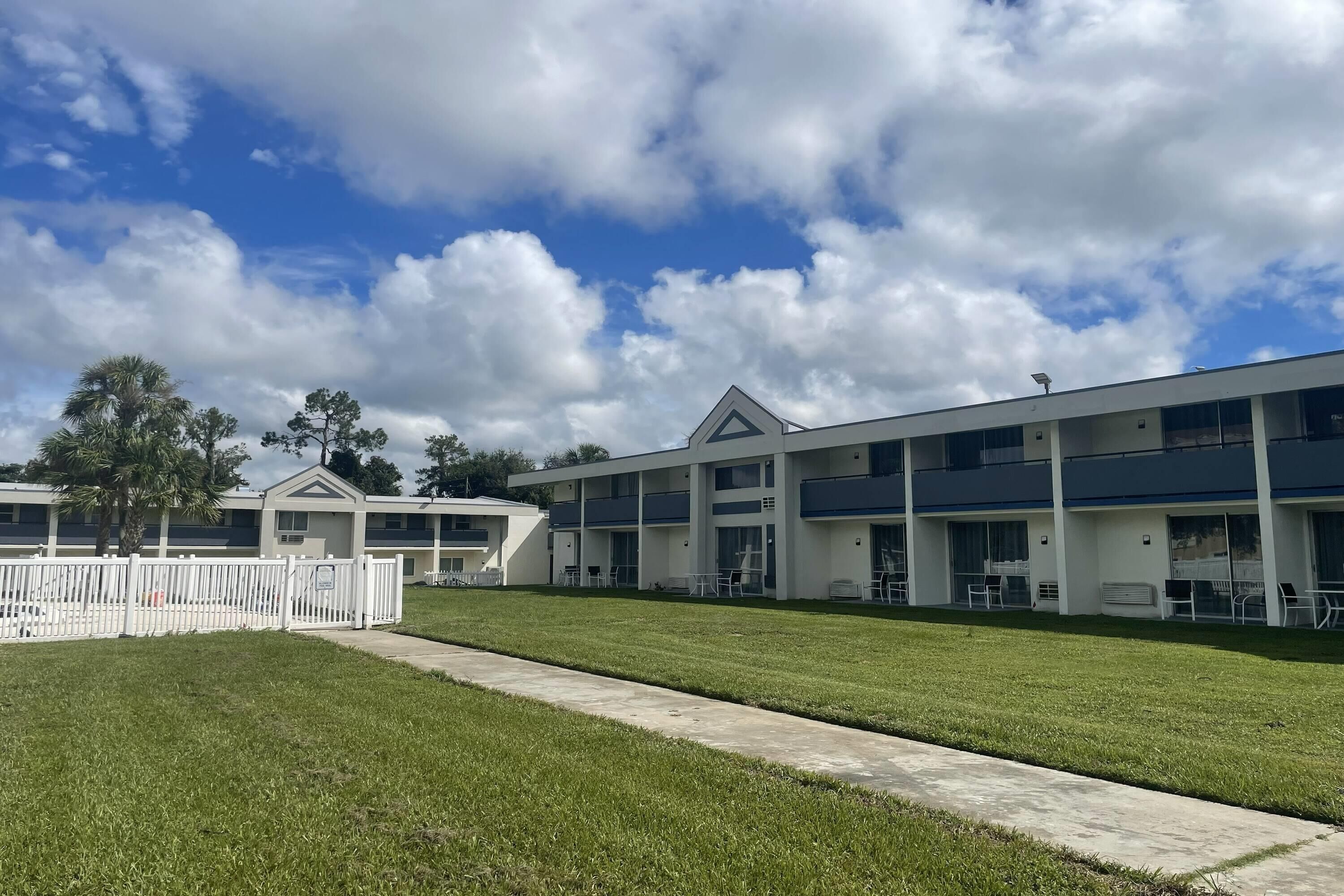 Un motel moderne, composé d’un bâtiment à deux étages, d’un espace extérieur abrité avec des sièges et d’une pelouse bien entretenue.