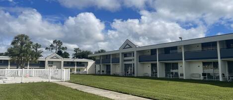 A modern motel with a two-story structure, a covered outdoor seating area, and a well-maintained lawn.