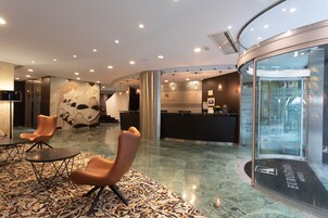 A lobby with a reception desk, seating area, and a glass elevator.