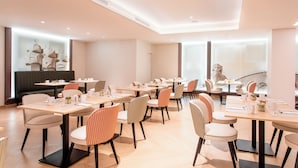 Un comedor moderno con varias mesas y sillas, una amplia zona de estar y vistas de la ciudad a través de grandes ventanales.