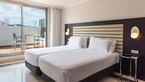 Habitación de hotel con dos camas, un balcón con mesa y sillas, y vista a la ciudad.