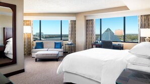 Habitación de hotel con una cama grande, un sofá, un escritorio y vistas a un paisaje urbano.