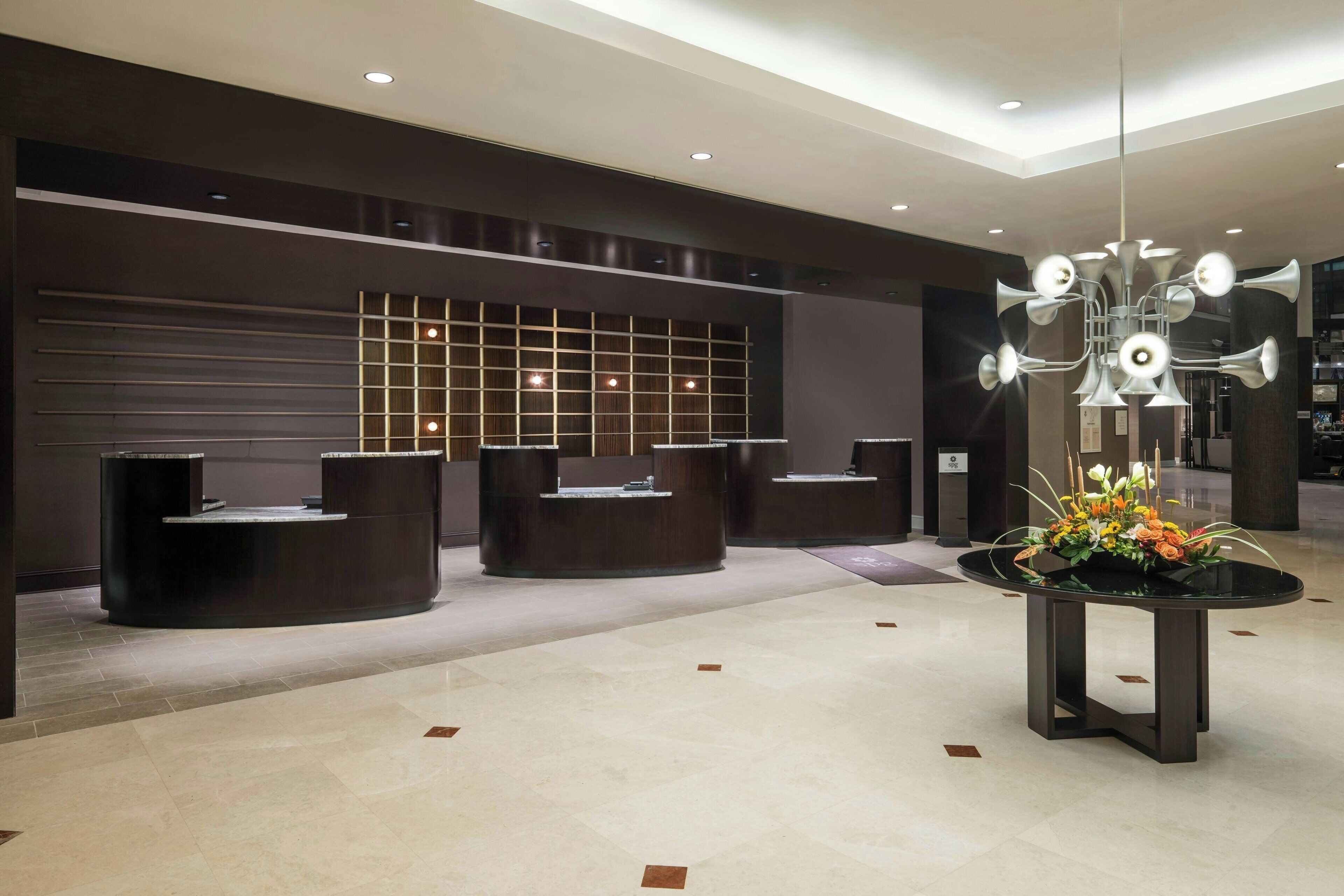 A modern reception area with three dark reception desks, a decorative light fixture, and a floral arrangement on a table.