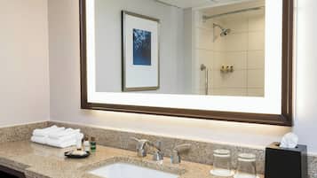 Un baño moderno con encimera de granito, un espejo grande, un lavabo y una zona de ducha visible en el reflejo.