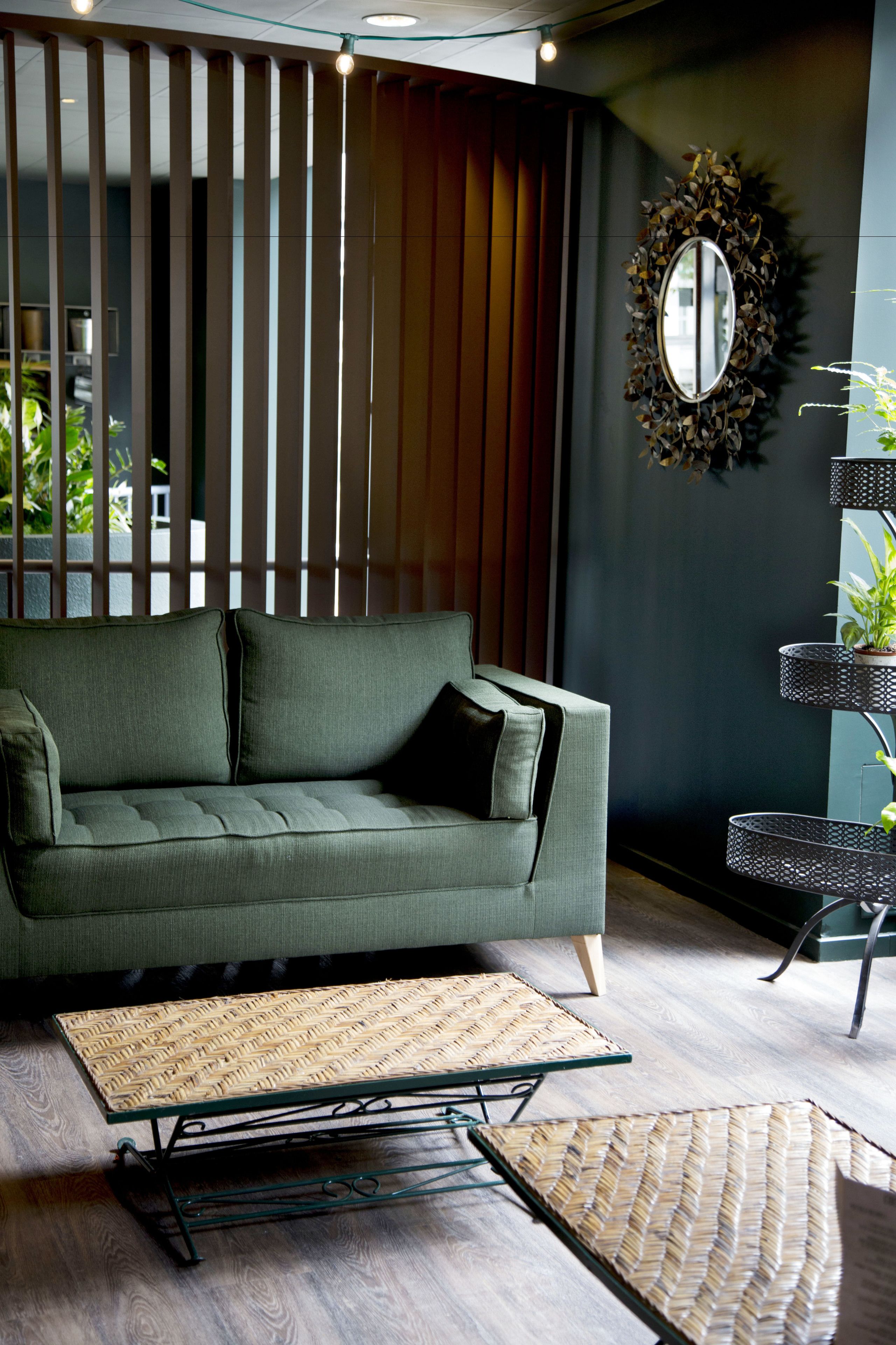 Una sala de estar moderna con un sofá verde, una mesa de centro tejida y un espejo decorativo en la pared.
