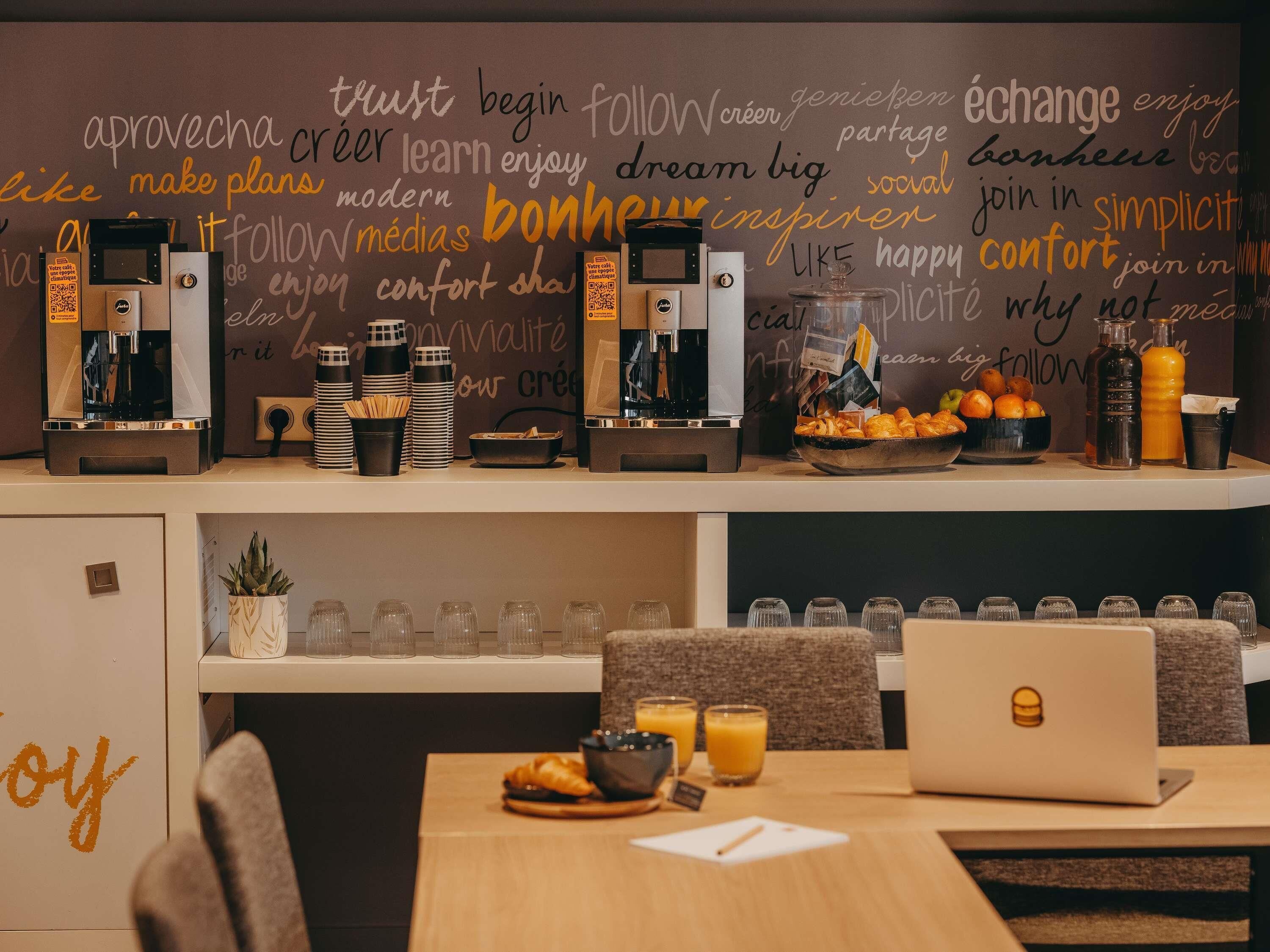 Una cafetería con máquinas de espresso, un bol de croissants y un ordenador portátil sobre la mesa.