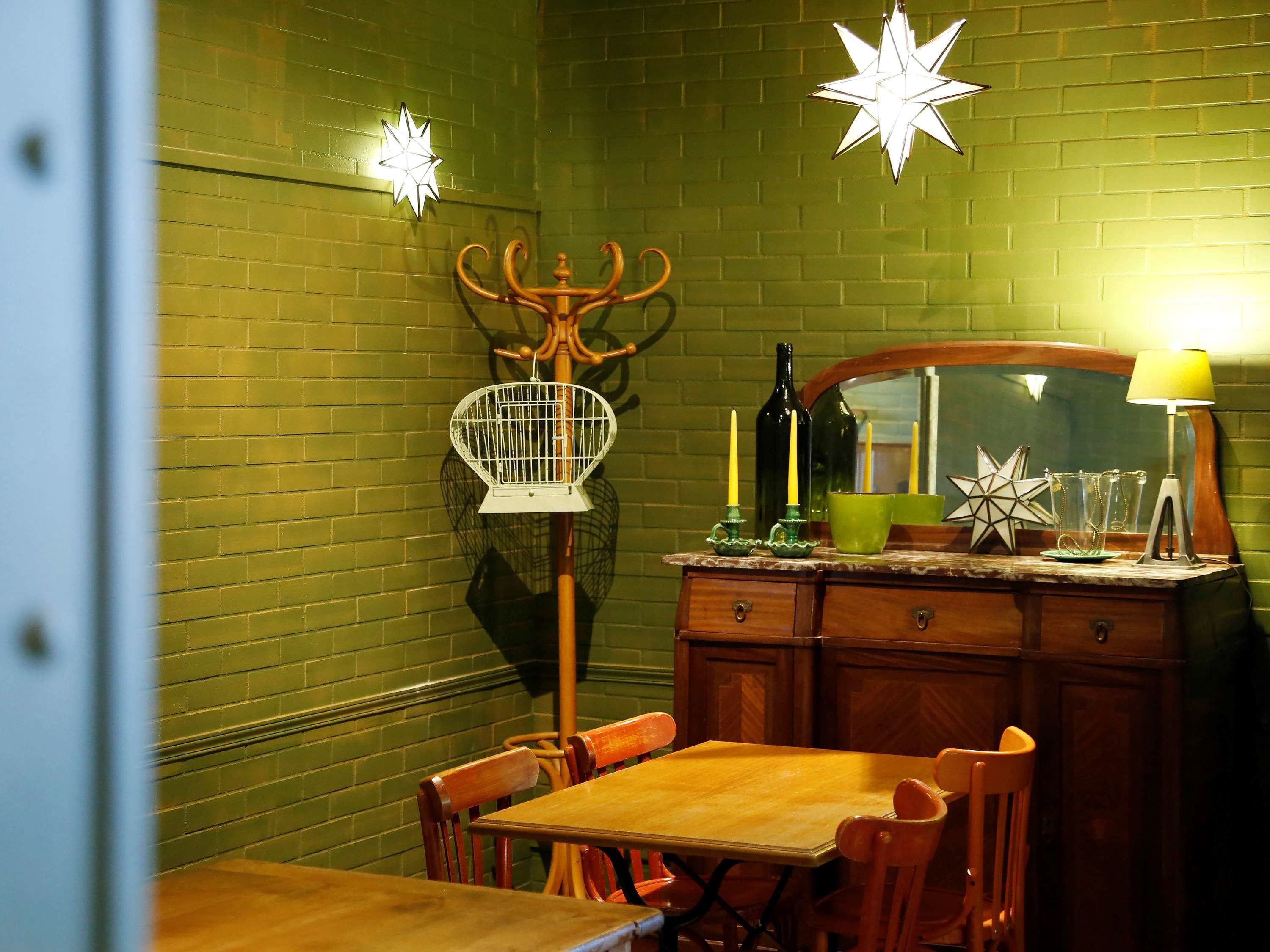 Un área de comedor con una mesa y sillas de madera, un muro de ladrillo verde y luces decorativas con forma de estrella.