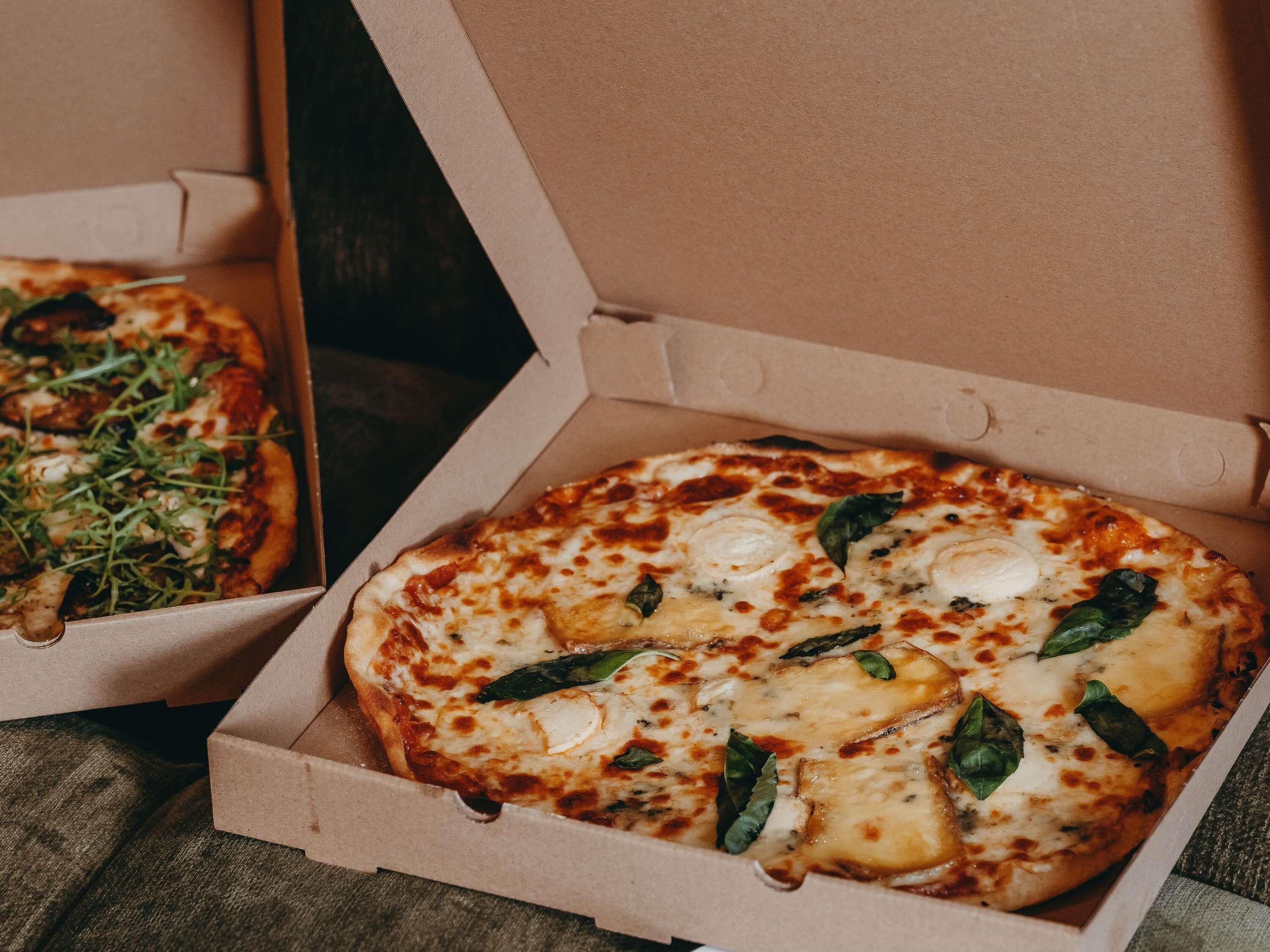 Two open pizza boxes with cheese and basil toppings.